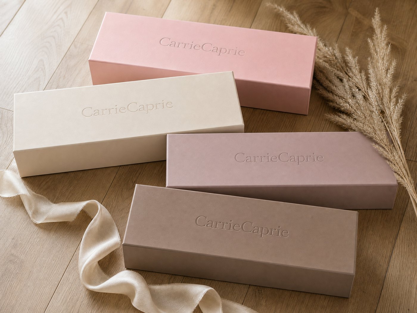 All four CarrieCaprie gift box colors — blush pink, champagne cream, dusty mauve, and soft cocoa taupe — displayed on a studio floor